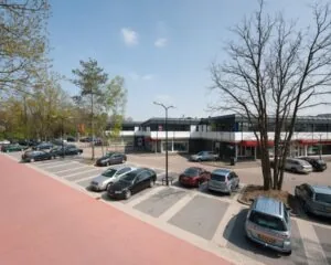 Parkeerterrein met geparkeerde auto's voor een laag kantoorgebouw op een zonnige dag.