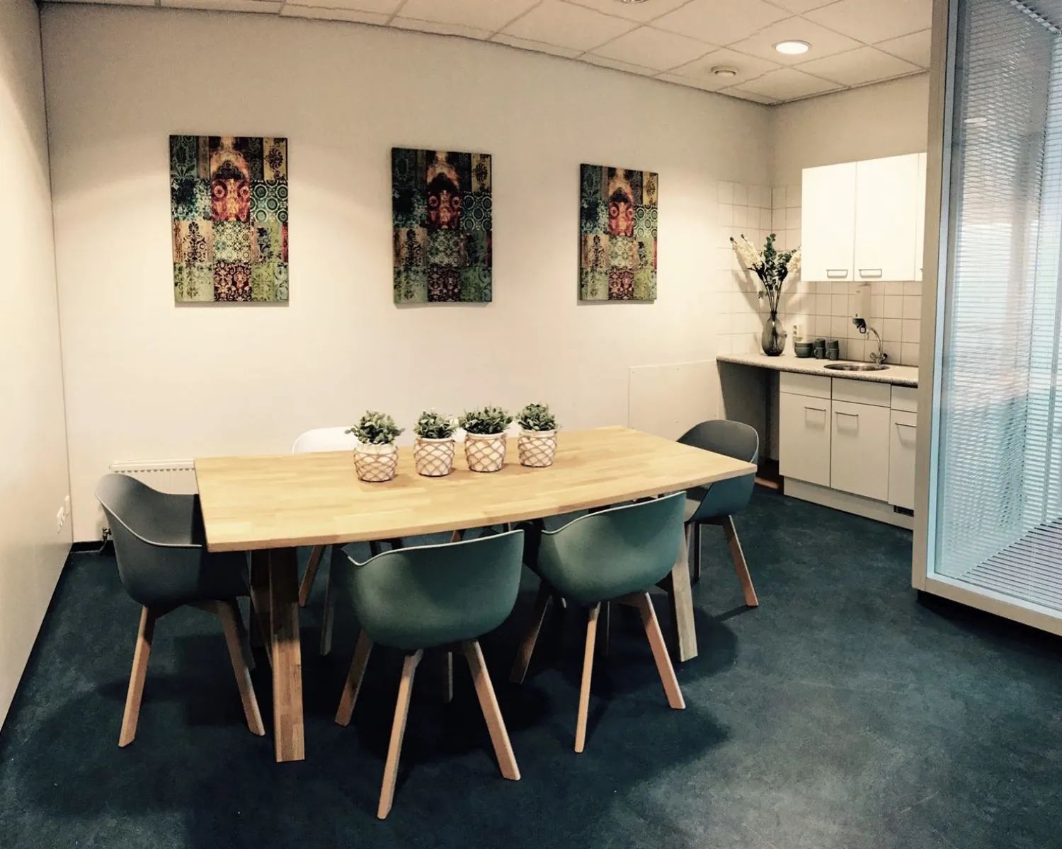 Moderne kantoor-pantry met houten tafel, zes stoelen, planten en wanddecoraties.