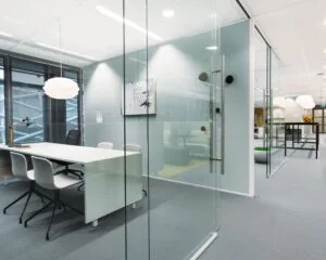 Moderne, glazen kantoorkamer met een witte vergadertafel, designverlichting en strakke inrichting.