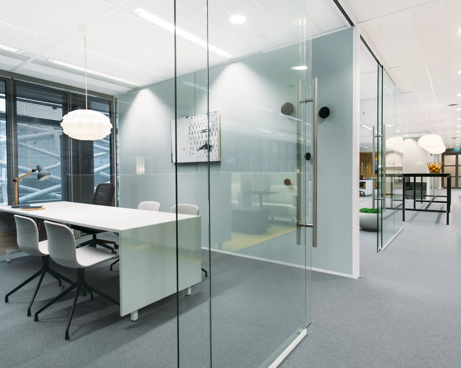 Moderne, glazen kantoorkamer met een witte vergadertafel, designverlichting en strakke inrichting.