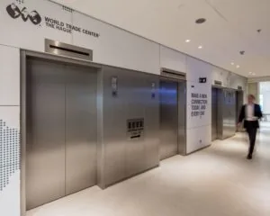 Hal met vier moderne liften in het World Trade Center The Hague, met een zakenman die voorbij loopt.