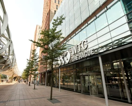 Ingang van het WTC The Hague met moderne glazen gevel en omliggende kantoorgebouwen.