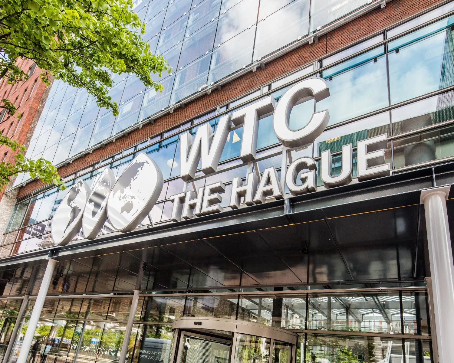 Ingang van het World Trade Center The Hague met groot logo en glazen gevel.