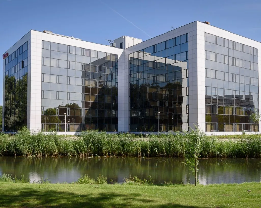 Modern kantoorgebouw met spiegelende glazen gevels aan het water, onder een blauwe lucht.