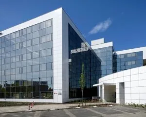 Modern kantoorgebouw met witte gevelpanelen en spiegelende ramen onder een heldere blauwe lucht.