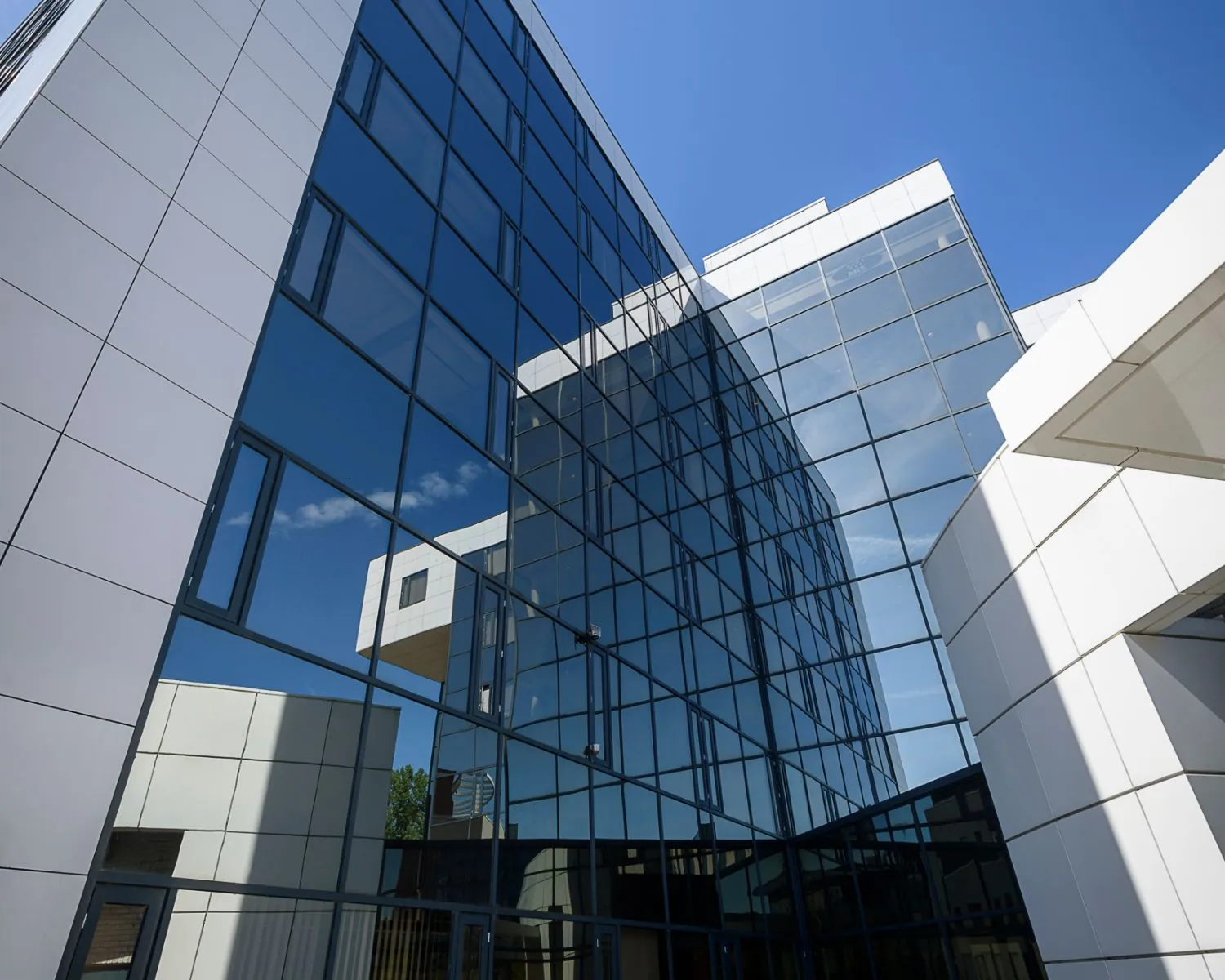 Modern kantoorgebouw met glazen gevels en witte panelen tegen een helderblauwe lucht.