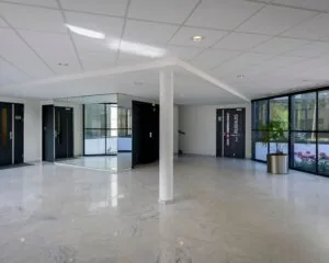 Lichte en moderne ontvangsthal met marmeren vloer, grote ramen, een spiegelwand en deuren naar vergaderruimtes in Het Ruighuis.