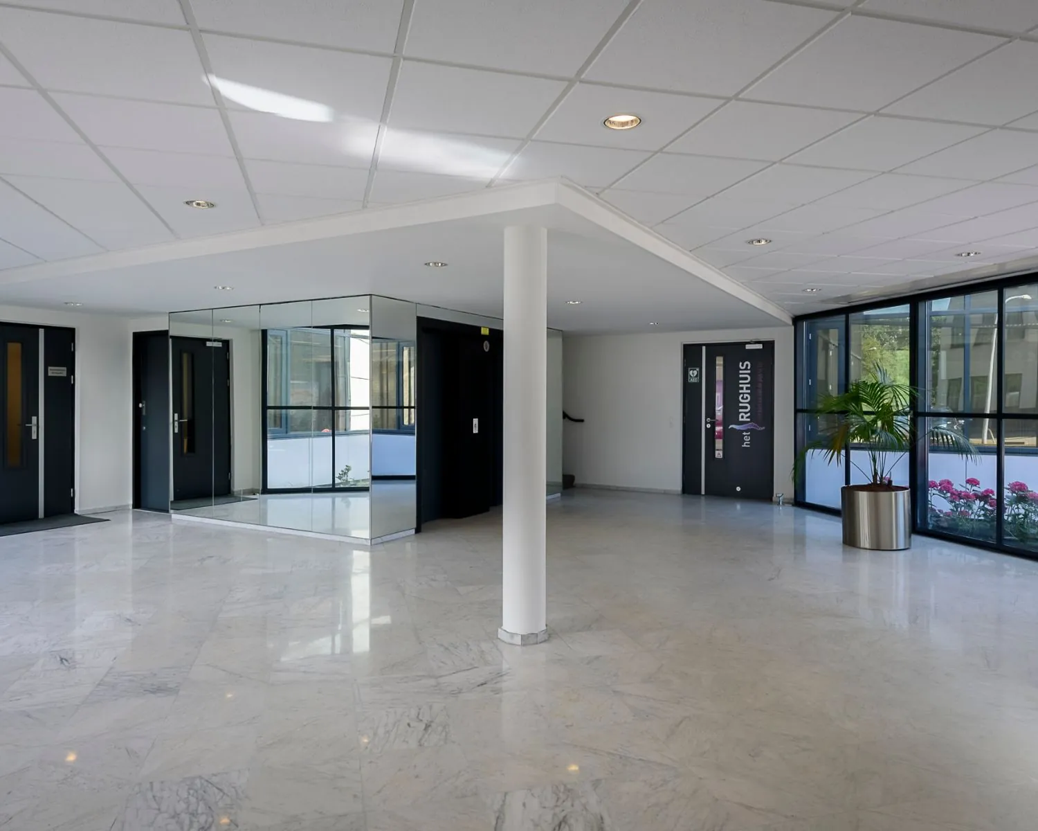 Lichte en moderne ontvangsthal met marmeren vloer, grote ramen, een spiegelwand en deuren naar vergaderruimtes in Het Ruighuis.