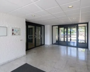 Inkomhal met marmeren vloer, witte muren en dubbele glazen toegangsdeuren.