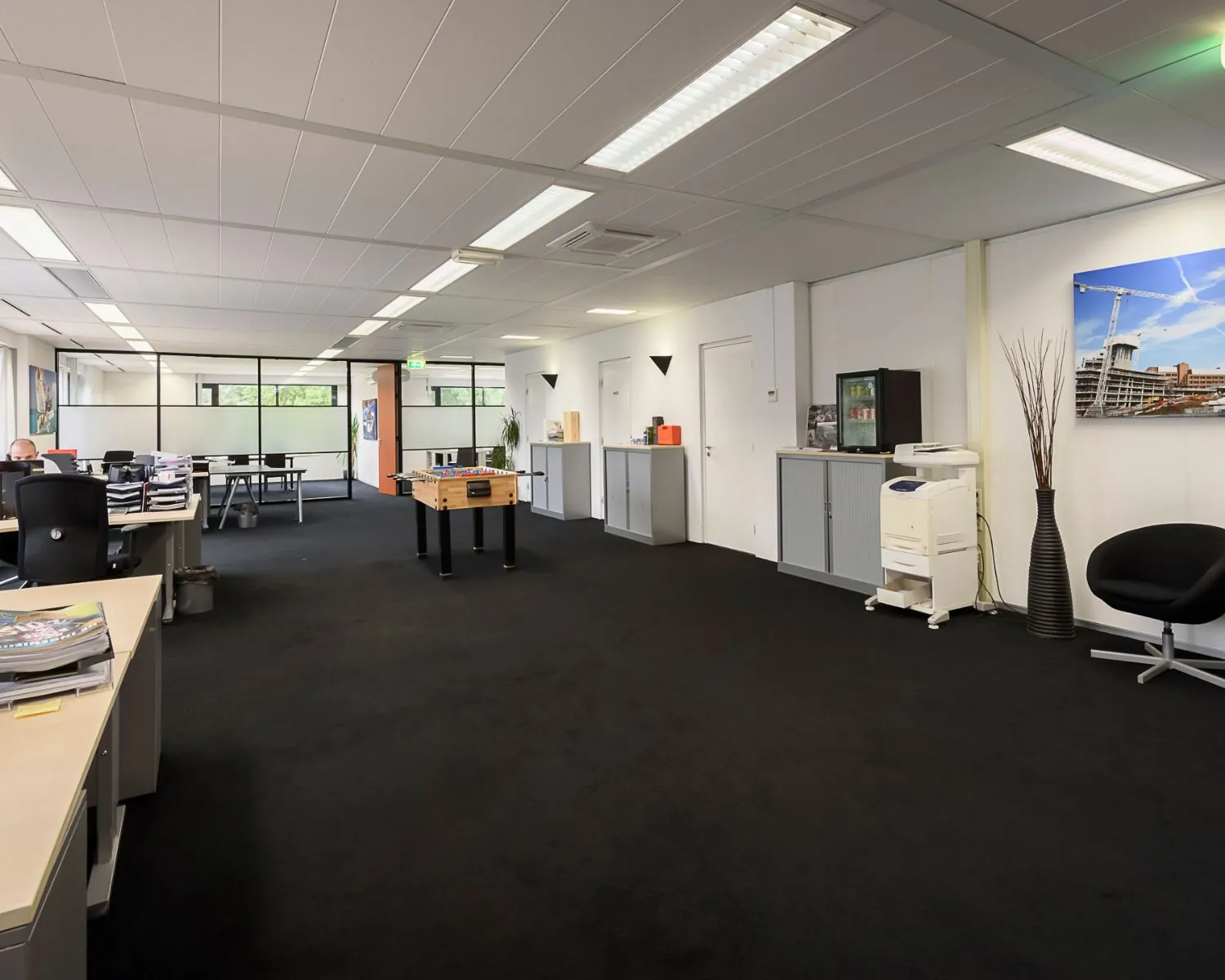 Ruim en modern kantoorinterieur met bureaus, een tafelvoetbaltafel, een printer en een zithoek.