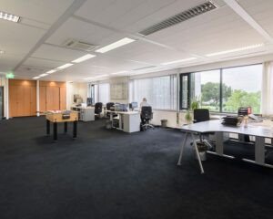 Ruim en licht modern kantoor met werkplekken, grote ramen en een tafelvoetbaltafel in het midden.