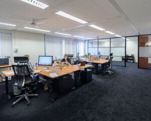 Moderne kantoorruimte met meerdere bureaus, computers en mensen die aan het werk zijn.