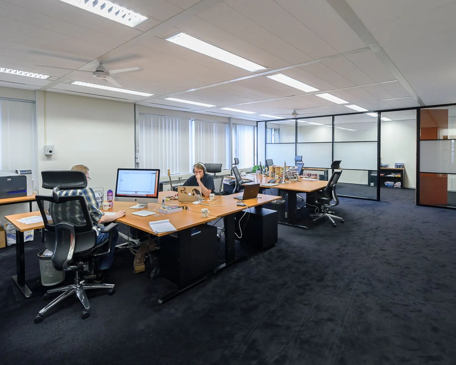 Moderne kantoorruimte met meerdere bureaus, computers en mensen die aan het werk zijn.