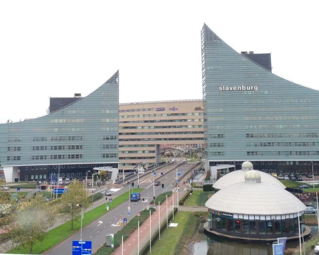 Twee moderne kantoorgebouwen met de naam 'Slavenburg' aan weerszijden van een drukke stadsweg in Rotterdam.