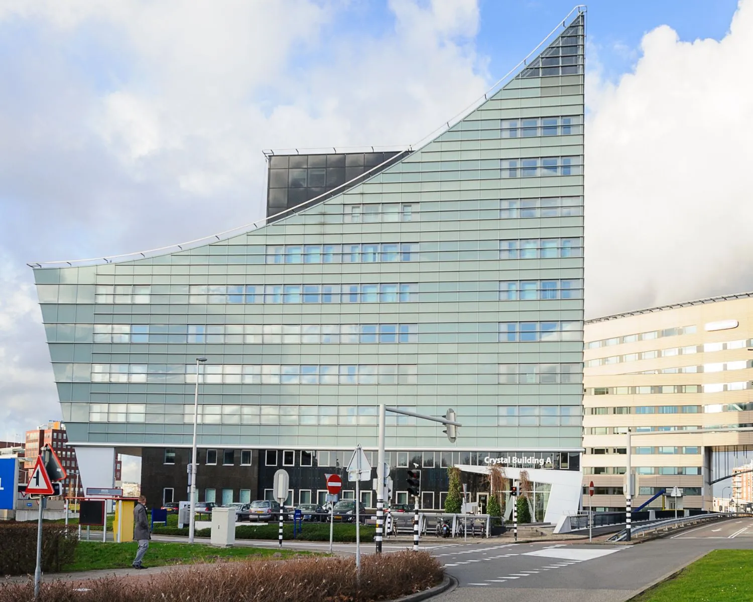 Modern kantoorgebouw met schuine glazen gevel, genaamd Crystal Building A, gelegen aan een rotonde.