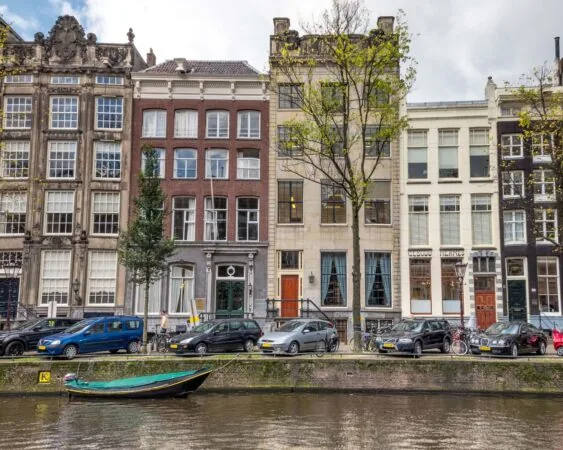 Gevels van historische grachtenpanden met geparkeerde auto's en een bootje aan een Amsterdamse gracht.
