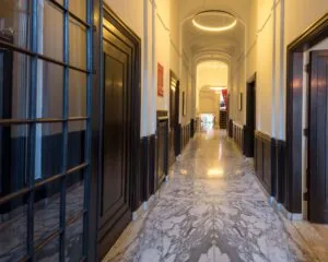 Elegante marmeren gang met hoge plafonds, houten deuren en een moderne ronde hanglamp.