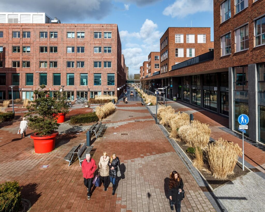 Winkelstraat met rode bakstenen gebouwen, brede voetgangerszone en mensen die langs het Spoorplein lopen.