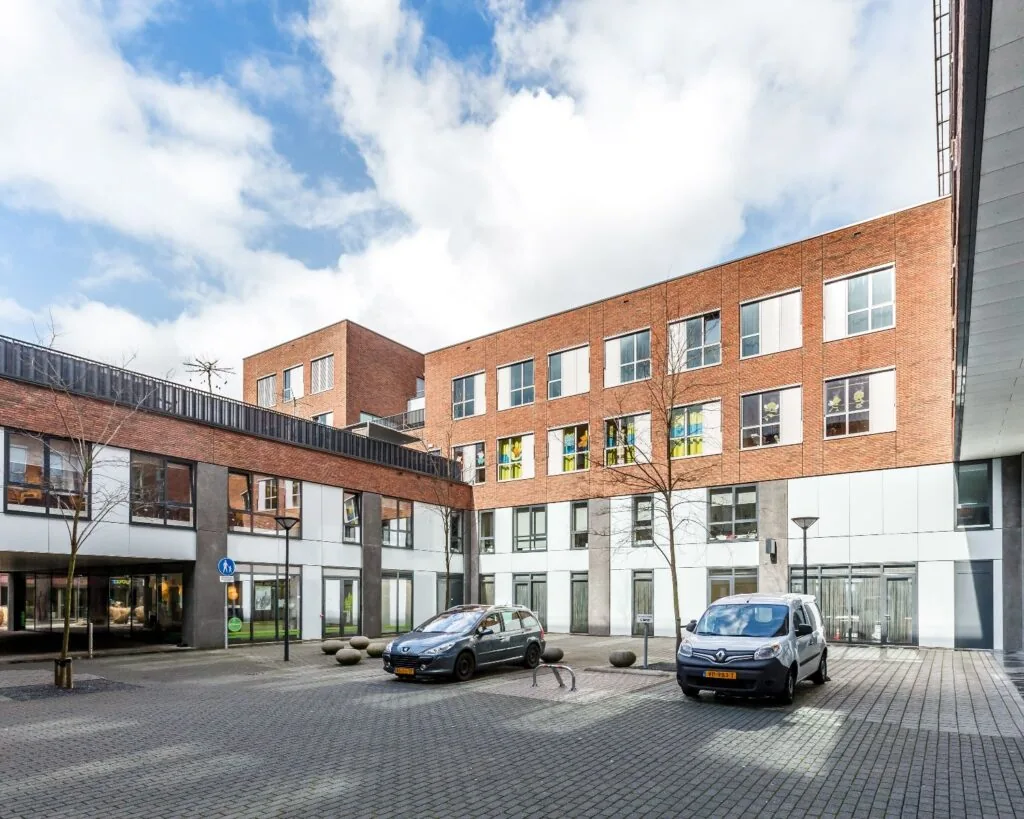 Binnenplaats van een modern woon- en kantoorgebouw met geparkeerde auto's en bakstenen gevel.