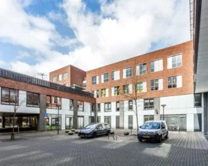 Binnenplaats van een modern woon- en kantoorgebouw met geparkeerde auto's en bakstenen gevel.
