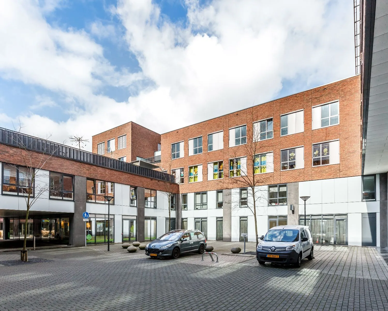 Binnenplaats van een modern woon- en kantoorgebouw met geparkeerde auto's en bakstenen gevel.