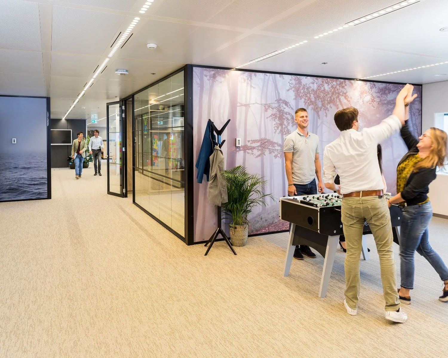 Kantoorruimte met medewerkers die tafelvoetbal spelen en anderen die door de gang lopen.