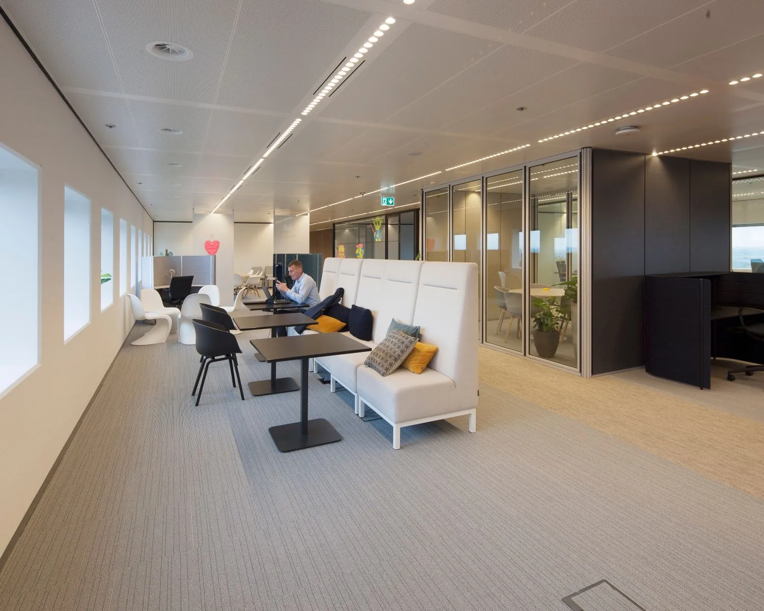Moderne kantoorspace met open werkplekken, glazen vergaderruimtes en een persoon werkend aan een tafel.