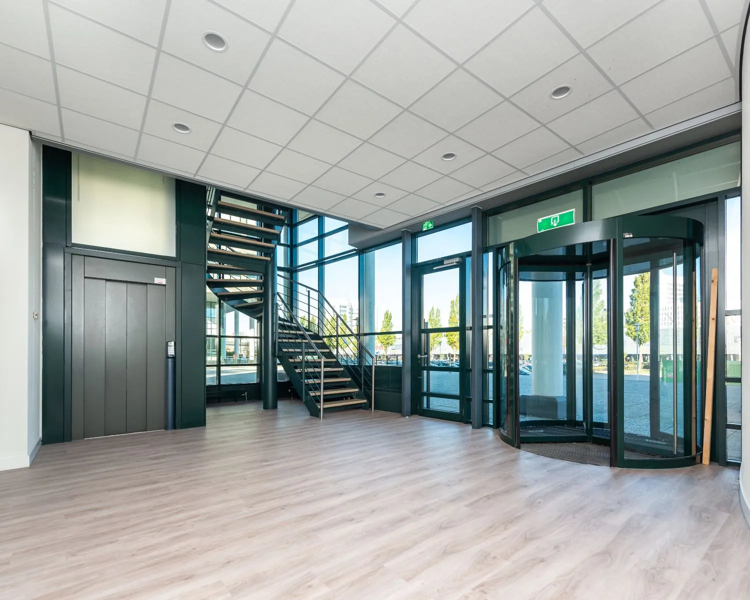 Modern bedrijfsentree met glazen draaideur, trap en lift in een lichte, open ruimte.