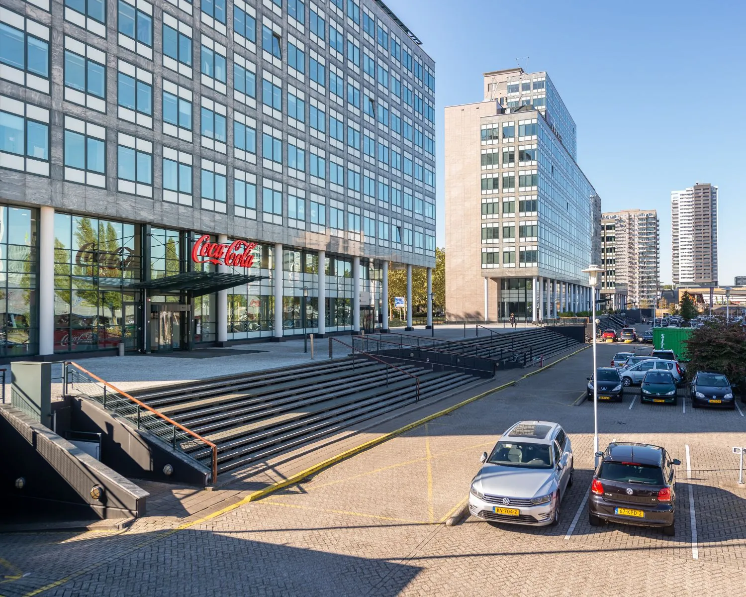 Kantoorgebouw met Coca-Cola-logo bij de ingang en parkeervakken op de voorgrond.