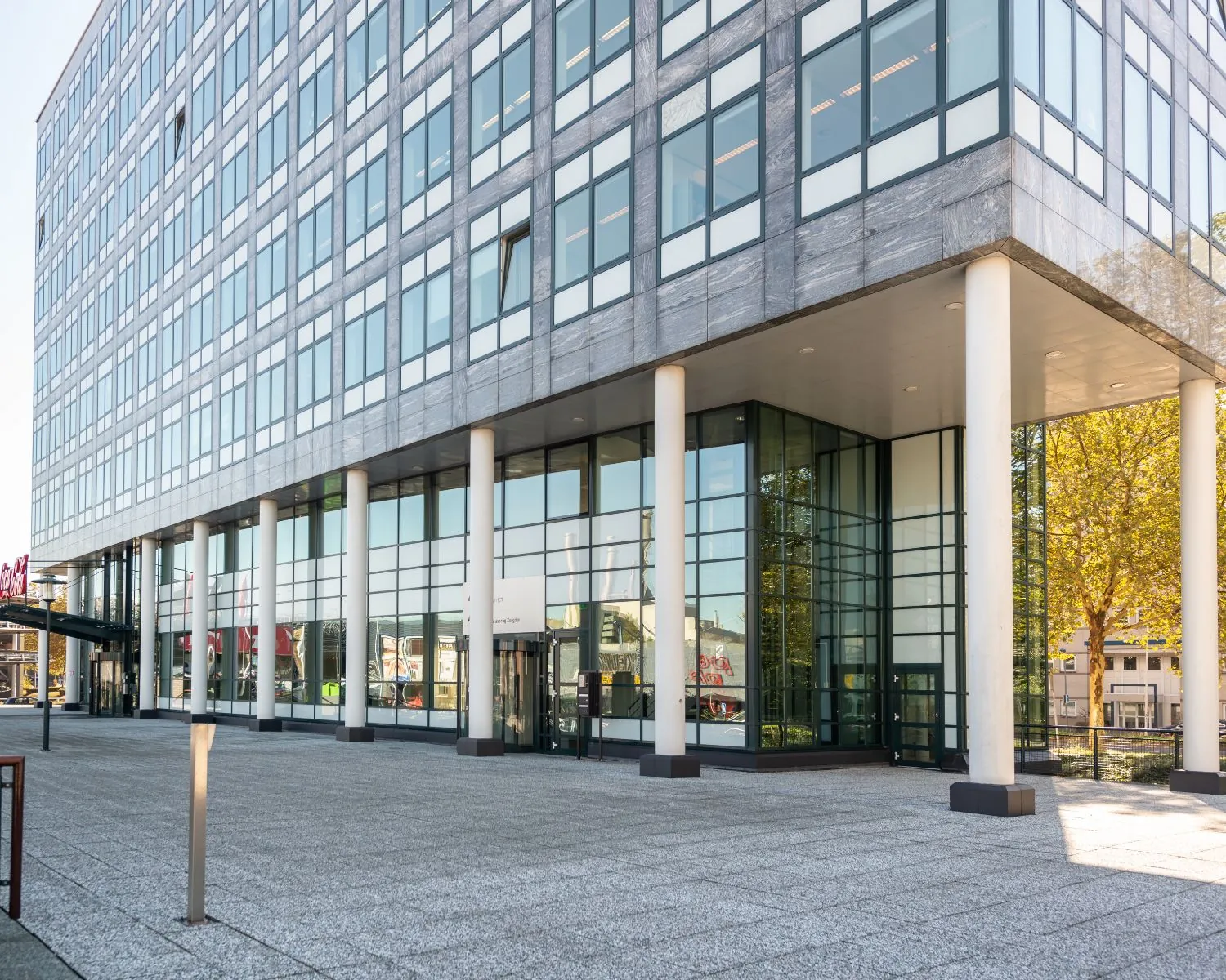 Moderne kantoorgebouw met glazen gevel en witte zuilen aan een open plein.