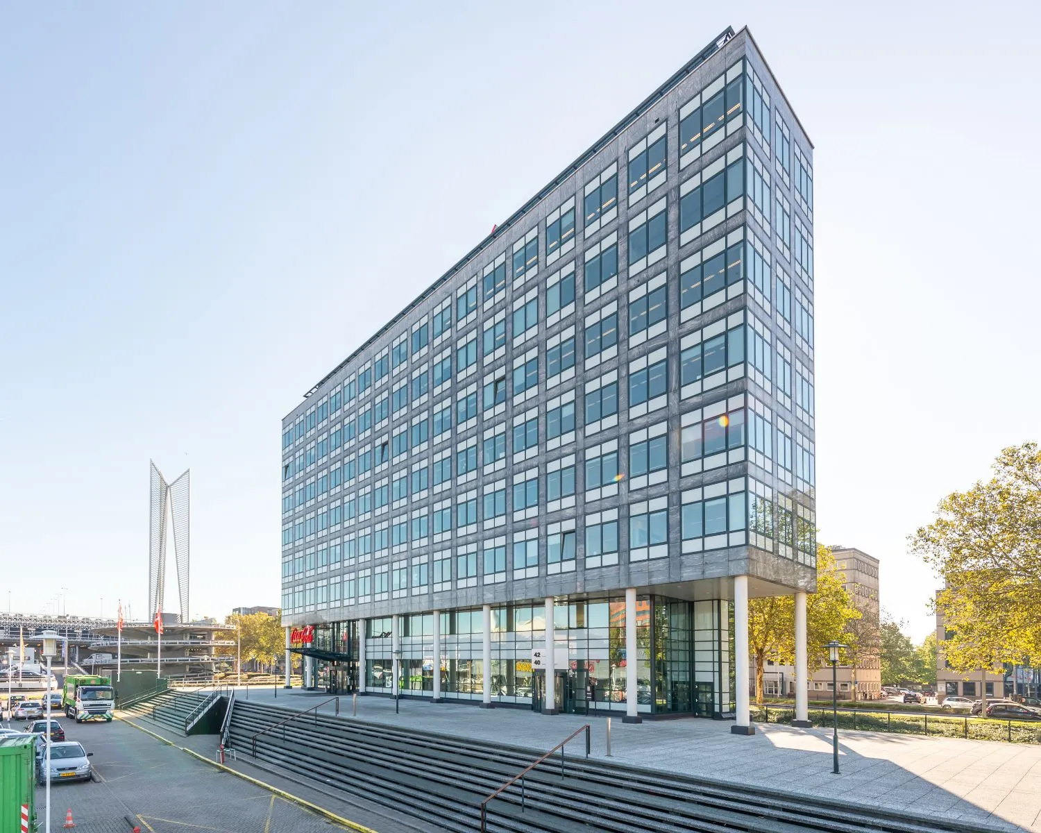 Modern kantoorgebouw met glazen gevel en trappen aan de voorzijde, gelegen in een stedelijke omgeving.