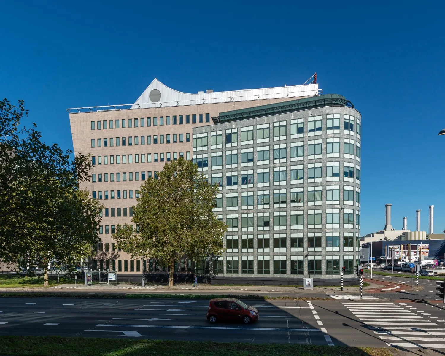Kantoorgebouw aan een kruispunt in een stedelijke omgeving met helderblauwe lucht.