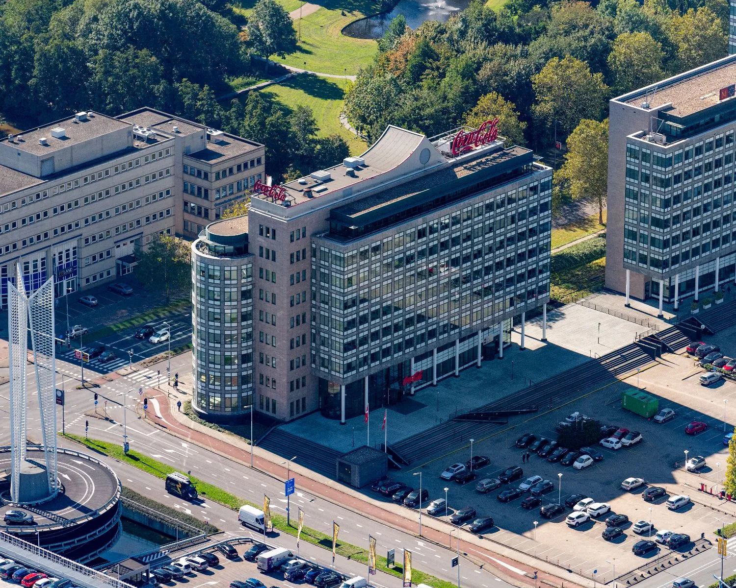 Luchtfoto van een kantoorgebouw met Coca-Cola-logo op het dak, omringd door wegen, auto’s en andere kantoren.