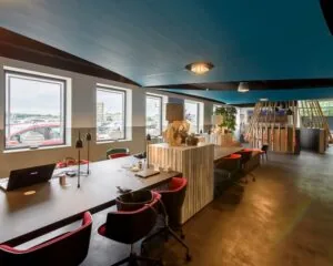Moderne, open kantoorruimte met werkplekken, designmeubilair en grote ramen met uitzicht op de parkeerplaats.