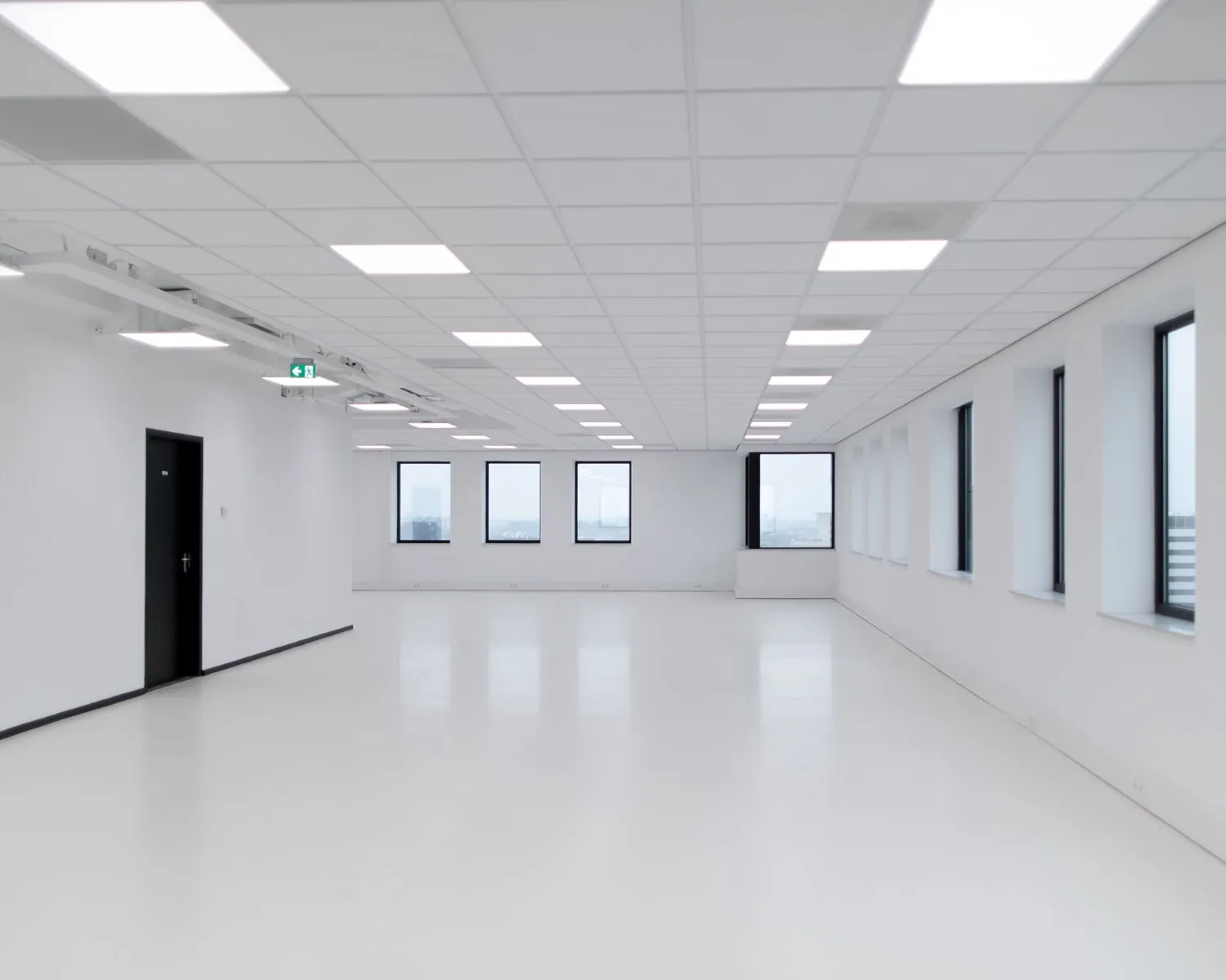 Lichte, lege kantoorruimte met witte muren, zwart-witte ramen en systeemplafond met LED-verlichting.