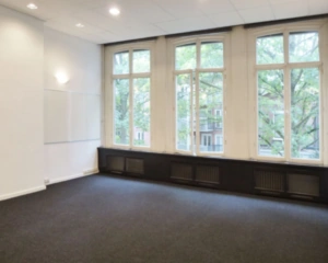 Lichte, lege vergaderruimte met grote ramen en een whiteboard aan de muur.