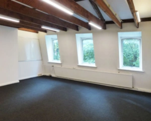 Leeg kantoor met zichtbare houten balken, drie ramen en een whiteboard aan de muur.