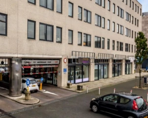 Ingang van parkeergarage Q-Park Amsterdamse Poort en naastgelegen winkelpanden aan een stadsstraat.