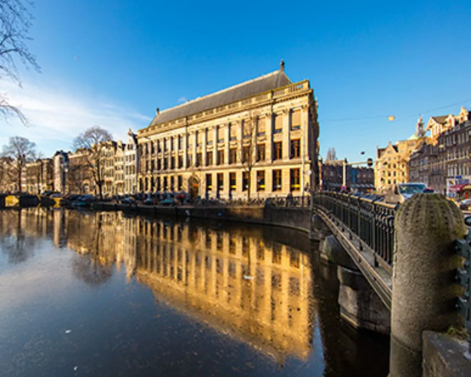 Een klassiek grachtenpand in Amsterdam weerspiegelt in het kalme water onder een heldere blauwe lucht.