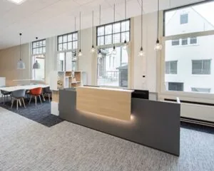 Moderne receptiebalie in een licht en ruim kantoor met grote ramen en stijlvolle hanglampen.