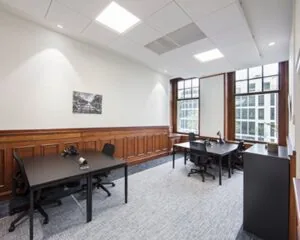 Licht en modern ingericht kantoor met vier bureaus, grote ramen en houten lambrisering.