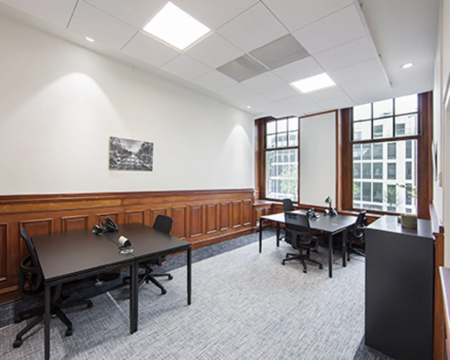 Licht en modern ingericht kantoor met vier bureaus, grote ramen en houten lambrisering.