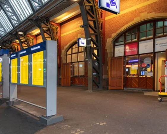 Ingang van een station met reisinformatieborden en de NS International Lounge.