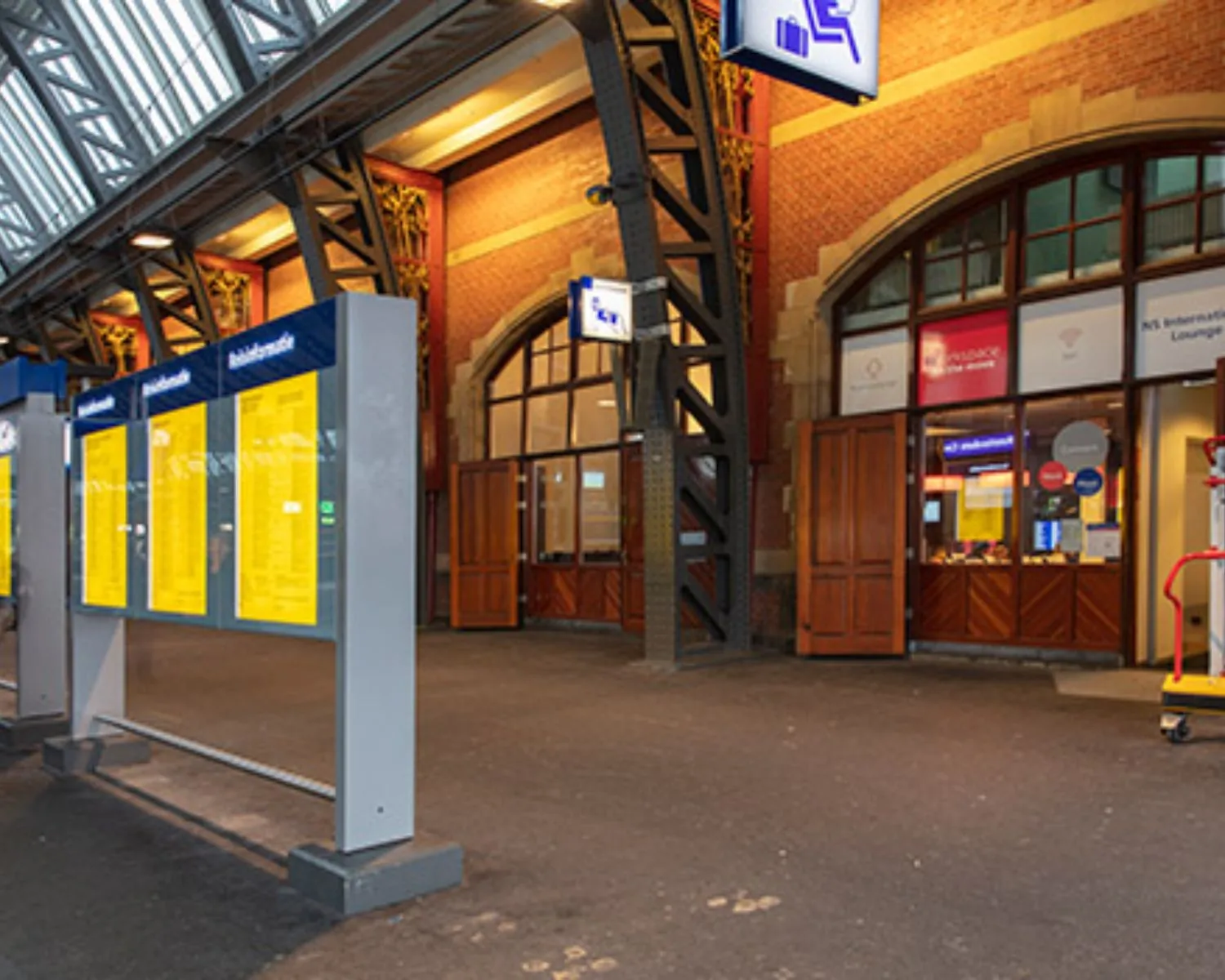 Ingang van een station met reisinformatieborden en de NS International Lounge.