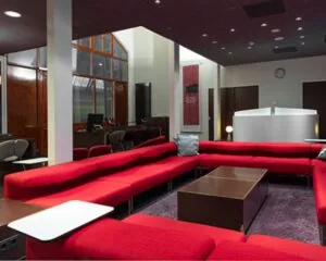Moderne lounge met rode banken, donkere houten accenten en een centraal ontvangstbalie in een zakelijke omgeving.