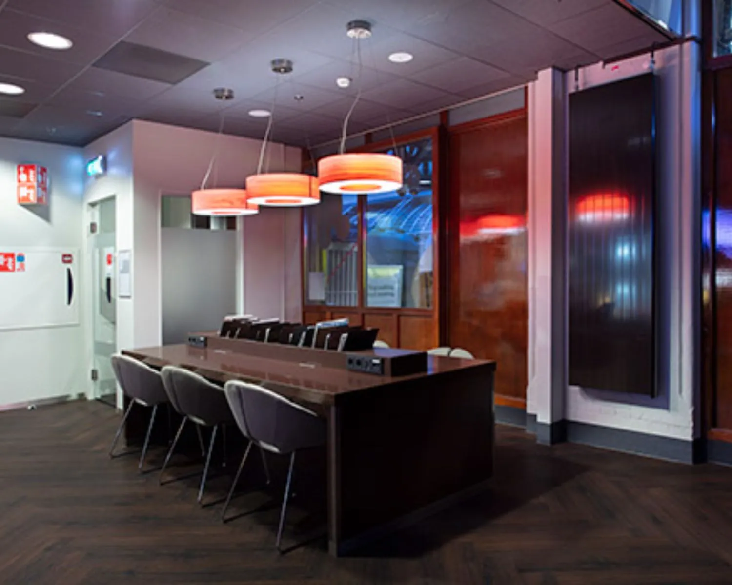 Moderne vergaderruimte met een lange tafel, comfortabele stoelen en hanglampen met rood licht.
