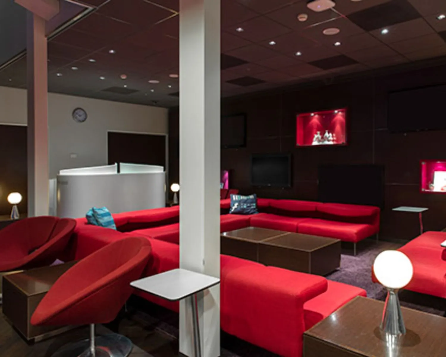 Moderne lounge met rode banken, donkere muren en sfeervolle verlichting.