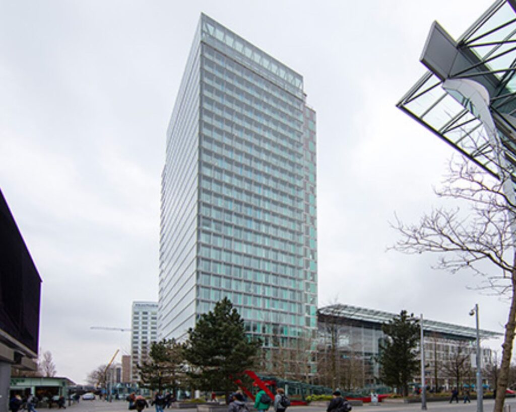 Hoog kantoorgebouw met glazen gevel in een stedelijke omgeving op een bewolkte dag.
