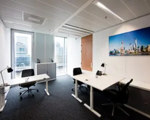 Modern ingericht kantoor met drie bureaus, zwarte bureaustoelen en een grote skylinefoto aan de muur.