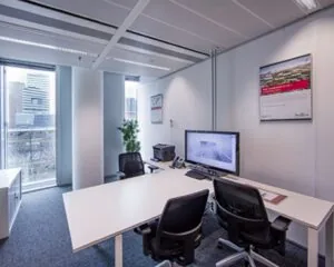 Modern ingericht kantoor met twee bureaustoelen, een bureau met computer en printer, en uitzicht op een stad met hoge gebouwen.